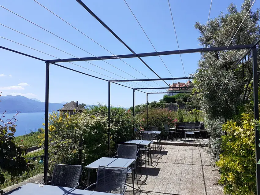 Pergola métallique au-dessus d'une terrasse avec tables, vue sur le lac