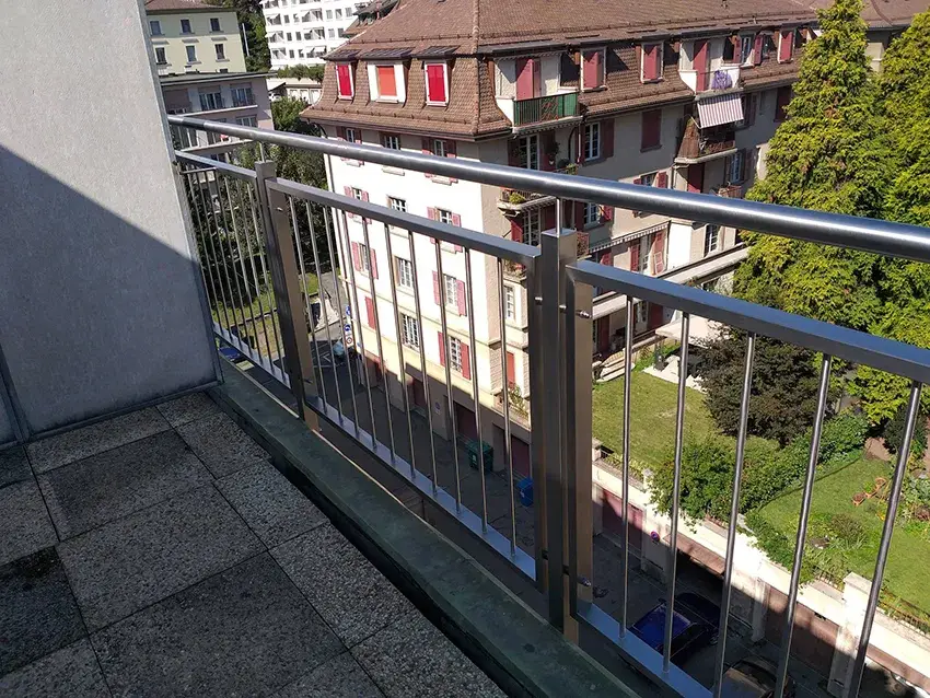 Garde-corps de balcon en inox à barreaux verticaux, vue sur un quartier d'immeubles