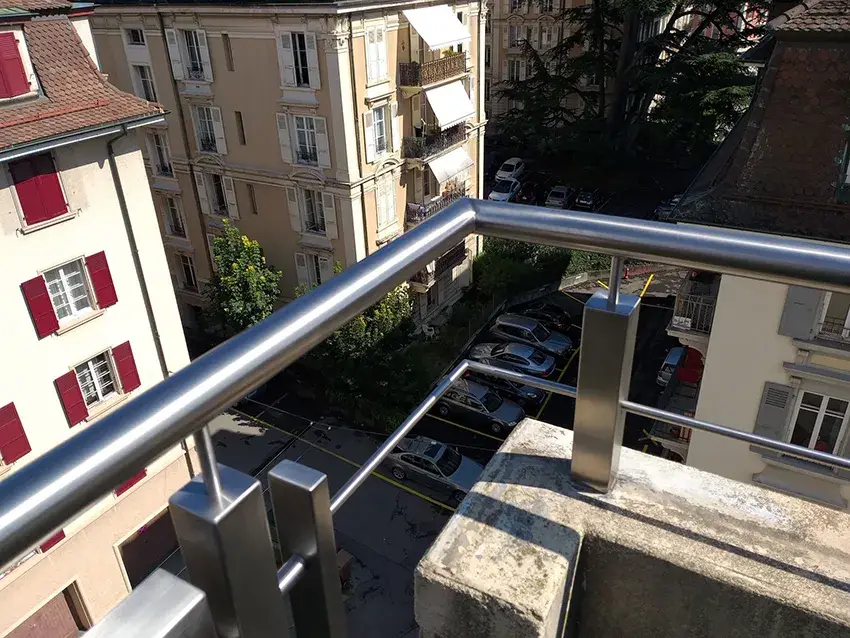 Main courante ronde en inox sur un balcon d'angle, au-dessus d'un parking