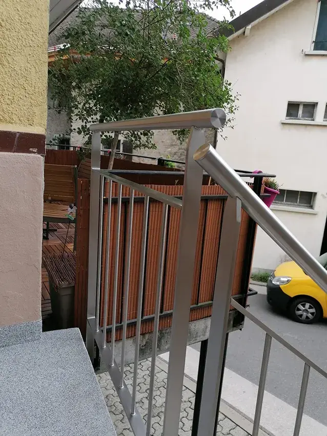 Garde-corps en inox avec main courante devant une palissade en bois