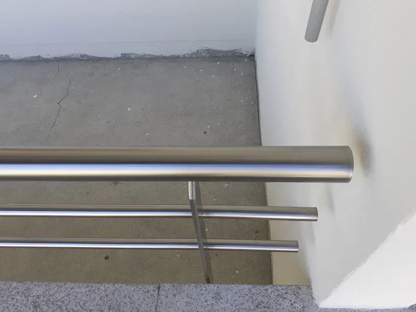 Détail d'une main courante et de lisses horizontales en inox contre un mur